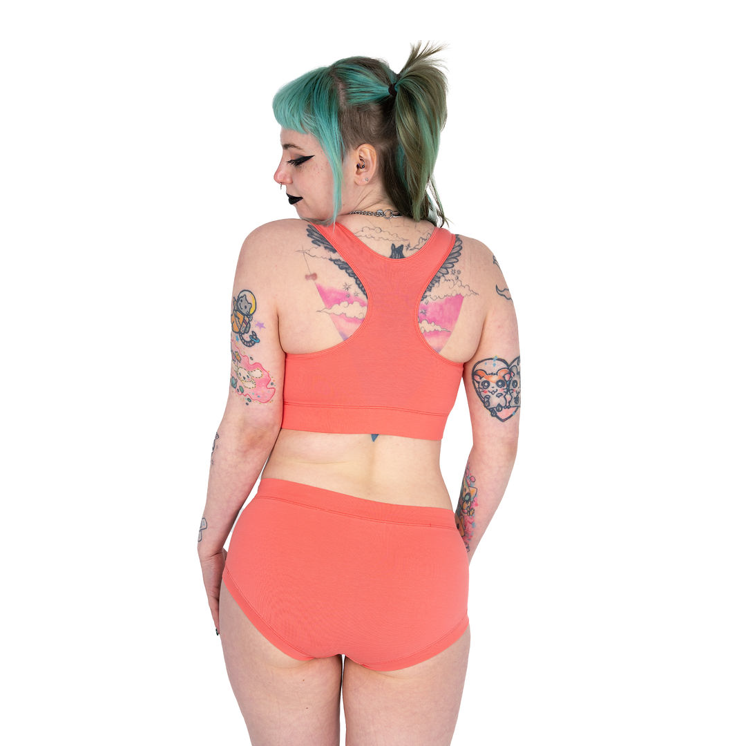 Back view of Faeryn wearing a coral racerback bralette and mid rise cotton briefs