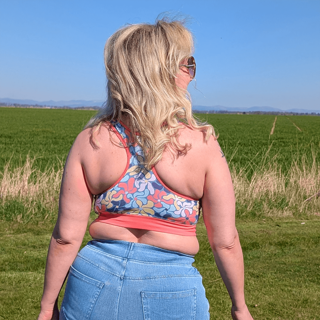 Ros is turned away, outside in the sunshine wearing a Wavy Flowers racerback bralette and jeans