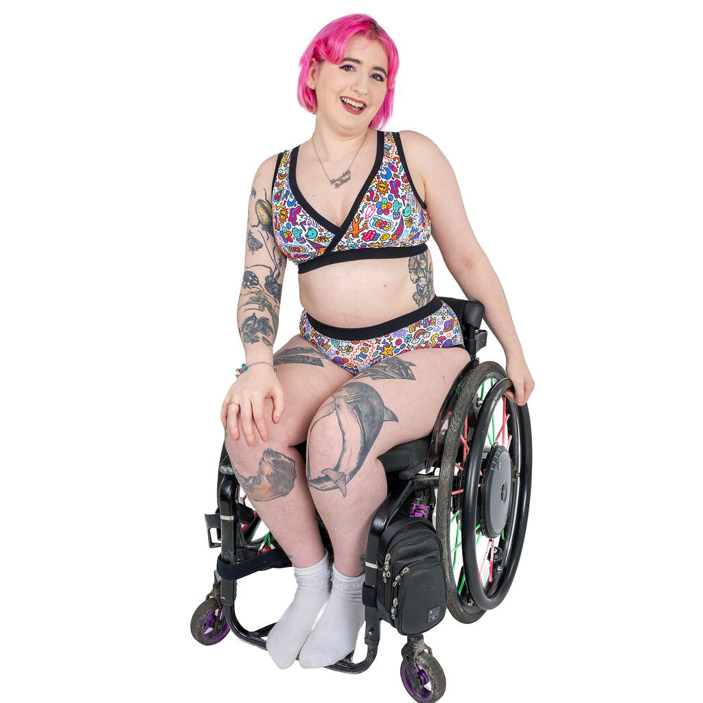 Eliza is sitting in their wheelchair wearing a Doodles underwear set 