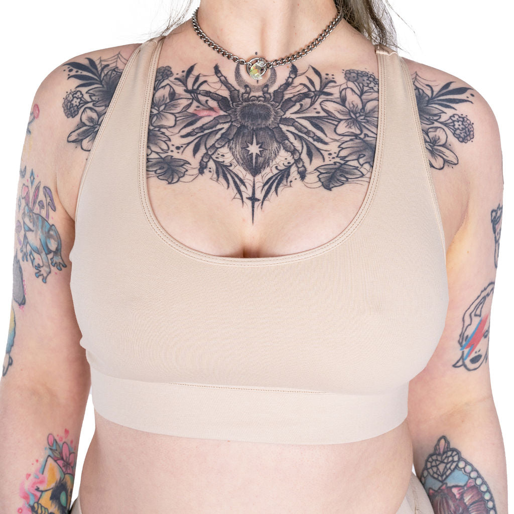 Person wearing a beige sports bra with floral and sun design tattoo on chest