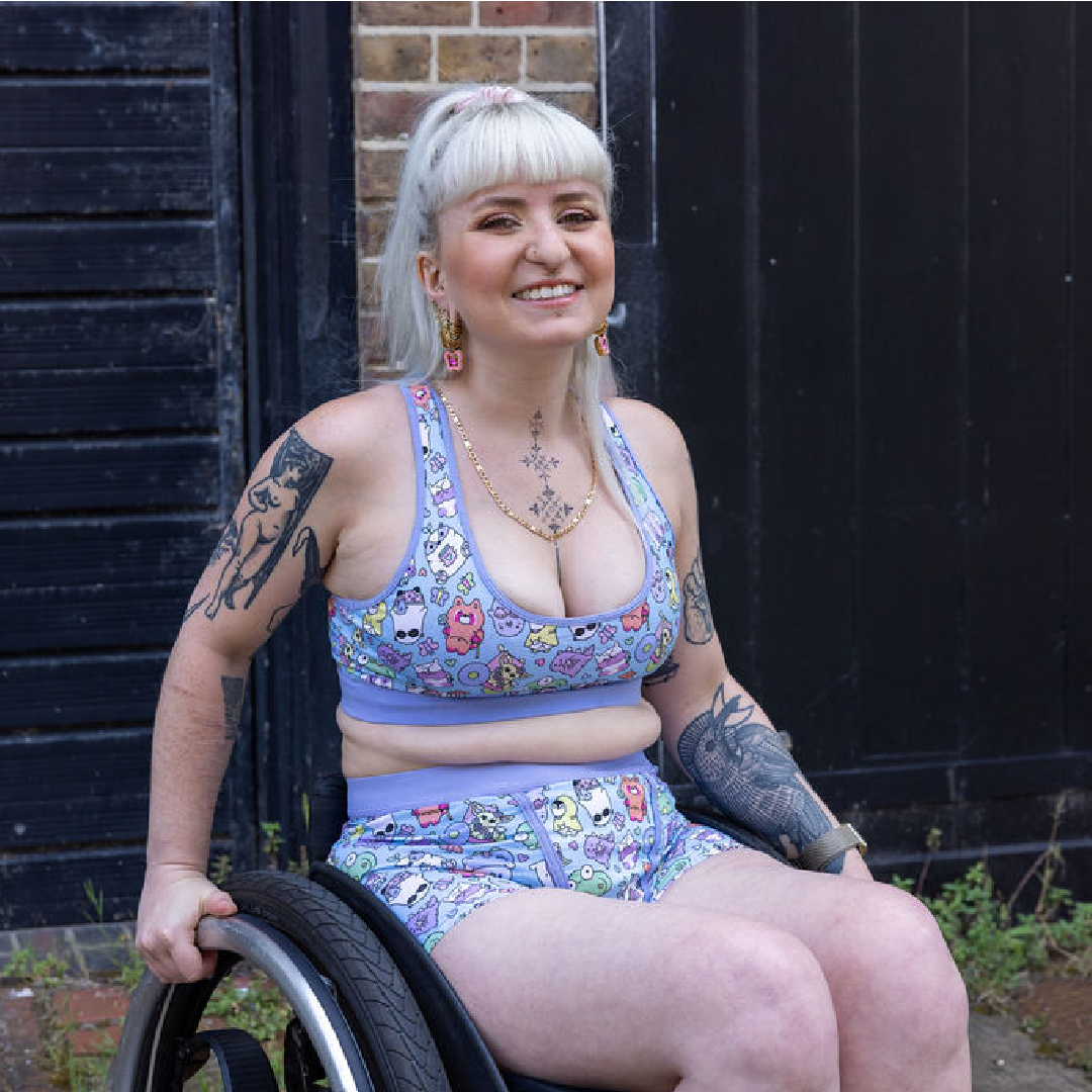 Jess is wearing a bralette and boxers sitting in her wheelchair out in a courtyard