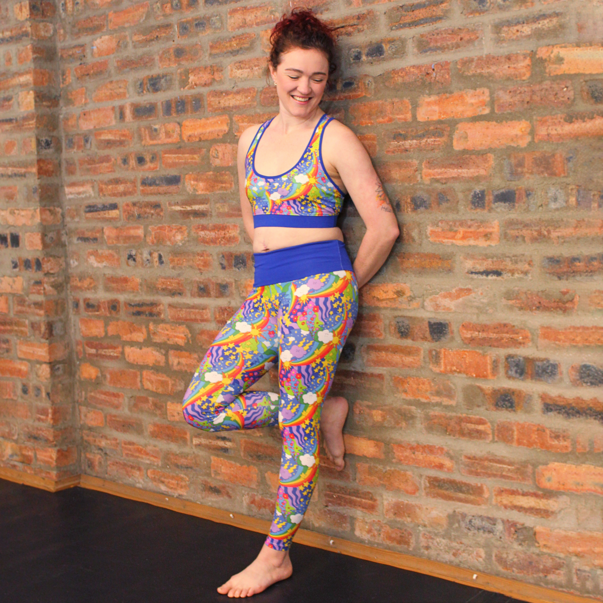 Jenni is wearing retro rainbows bright leggings and racerback bralette against an open brick wall