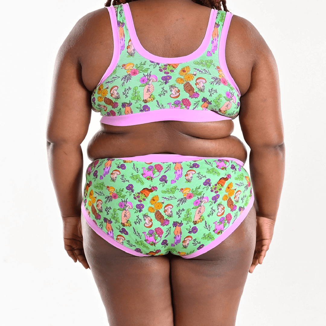 Back view of Kayla wearing mid rise briefs and bra in Secret Garden